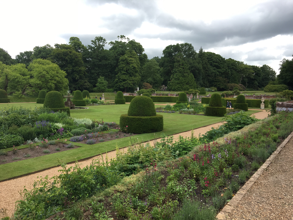 Formal gardens looking away from the house - gravel walkways, topisry snd long borders of flowers.