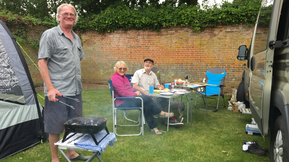 Kevin cooking on the BBQ while Di and David enjoy a drink sitting outside our vans.