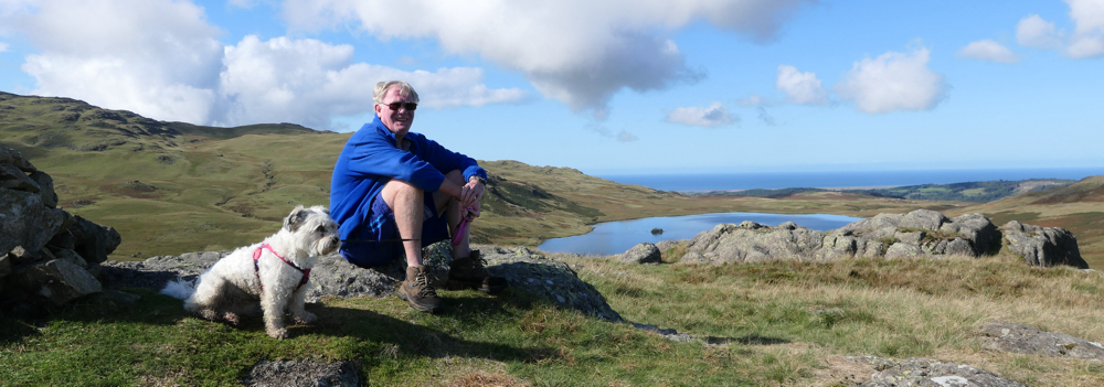 Kevin and Gracie sitting on a stone on the top of Devoke Seat with Devoke Water below.