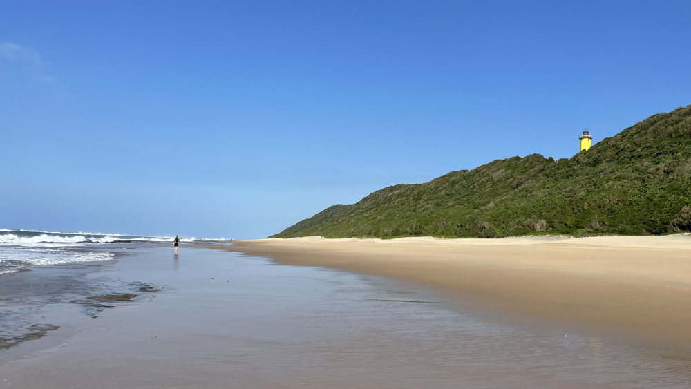 A nearly empty beach with the lighthouse on the dunes.