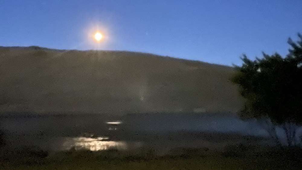 Full moon rising with its reflection in the dam.