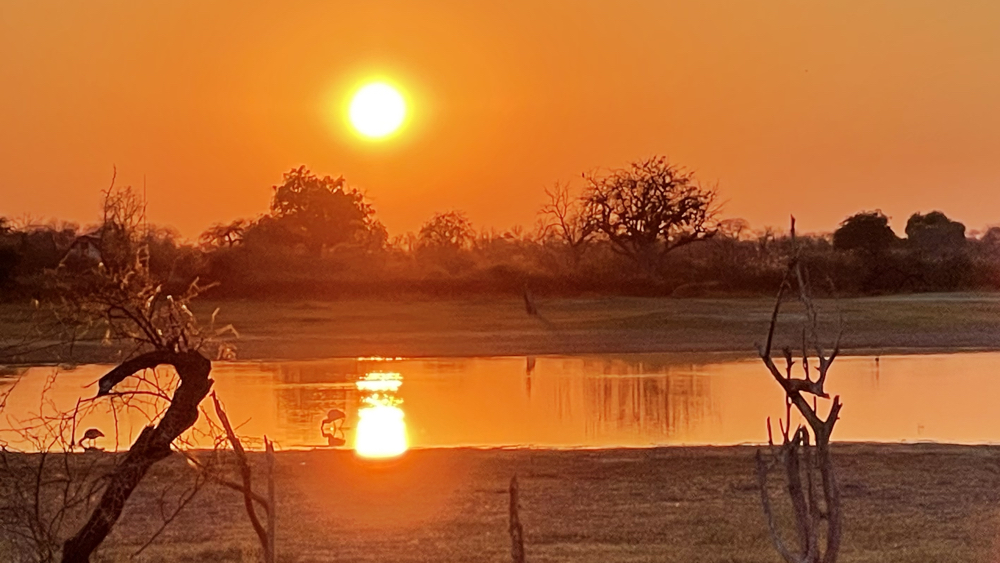 A bright orange sunrise over a small pan with the sun reflected in the water