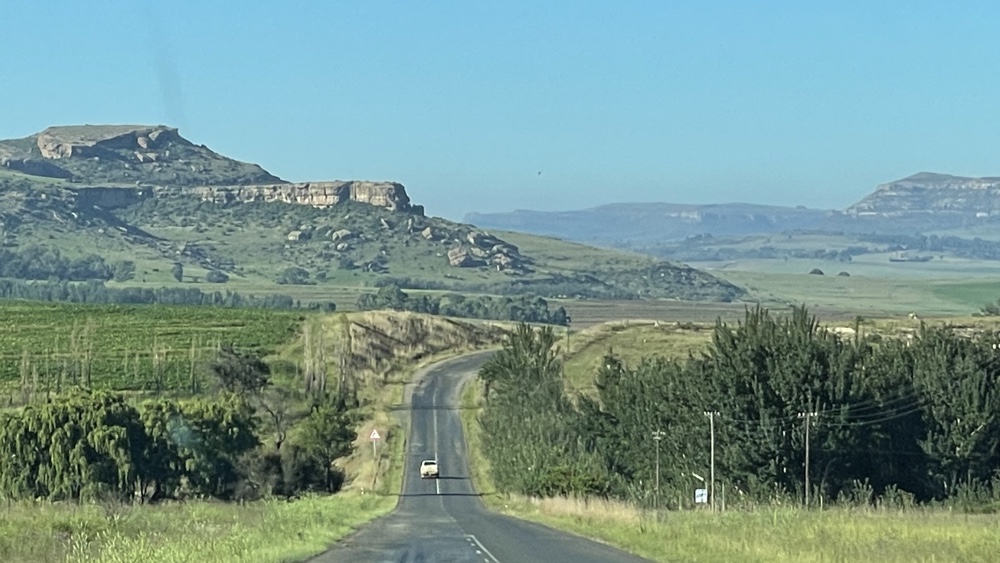 A road with green fields and mountains around.